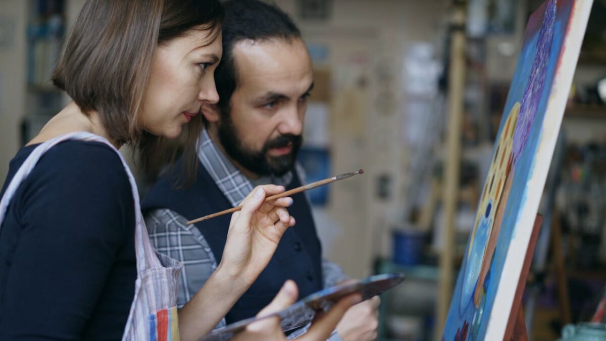 Two artists collaborate on a colorful painting in an art studio, demonstrating creative teamwork.